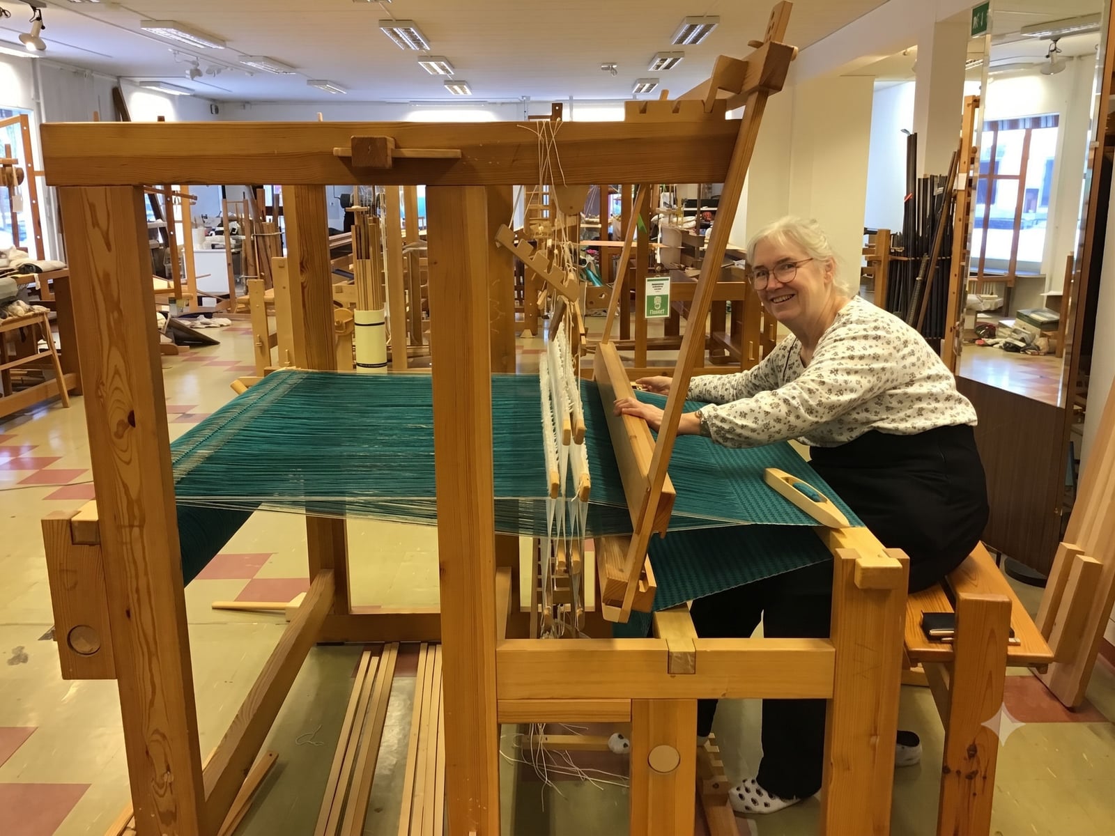 An instructor smiling at a large Swedish floor loom strung with teal warp threads